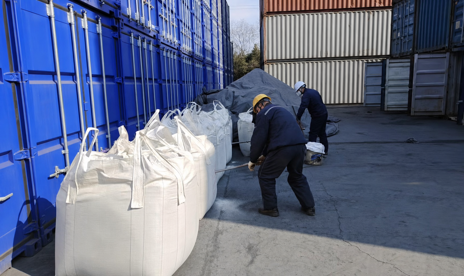 Mining supply-chain workers handling bulk material beside shipping containers